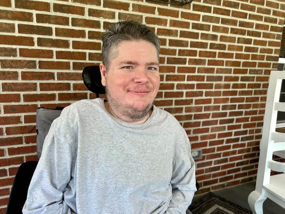 A photograph of me, a white man in his thirties, sitting in a wheelchair in front of a brick wall.